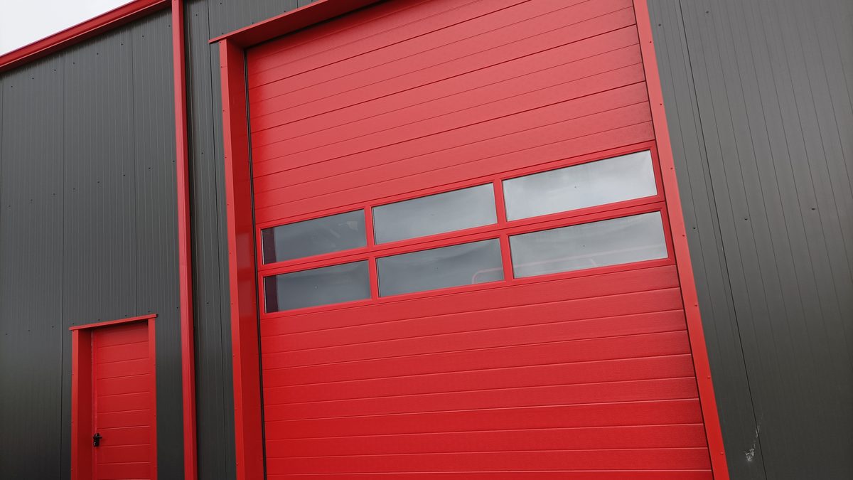 Porte sectionnelle industrielle ARIANE rouge avec portillon, sur un bâtiment d'activité