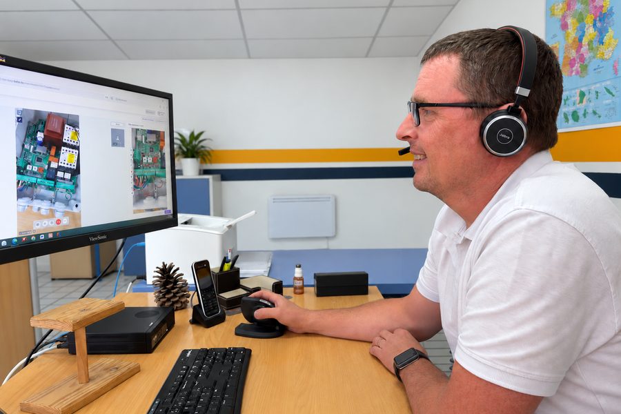 Technicien du service clientèle JAVEY au téléphone, casque sur les oreilles, devant l'écran de diagnostic d'une armoire de commande